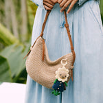 Crocheted shoulder bag in cream with brown leather straps, featuring crocheted flower and leaf decorative elements.