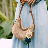 Crocheted shoulder bag in cream with brown leather straps, featuring crocheted flower and leaf decorative elements.